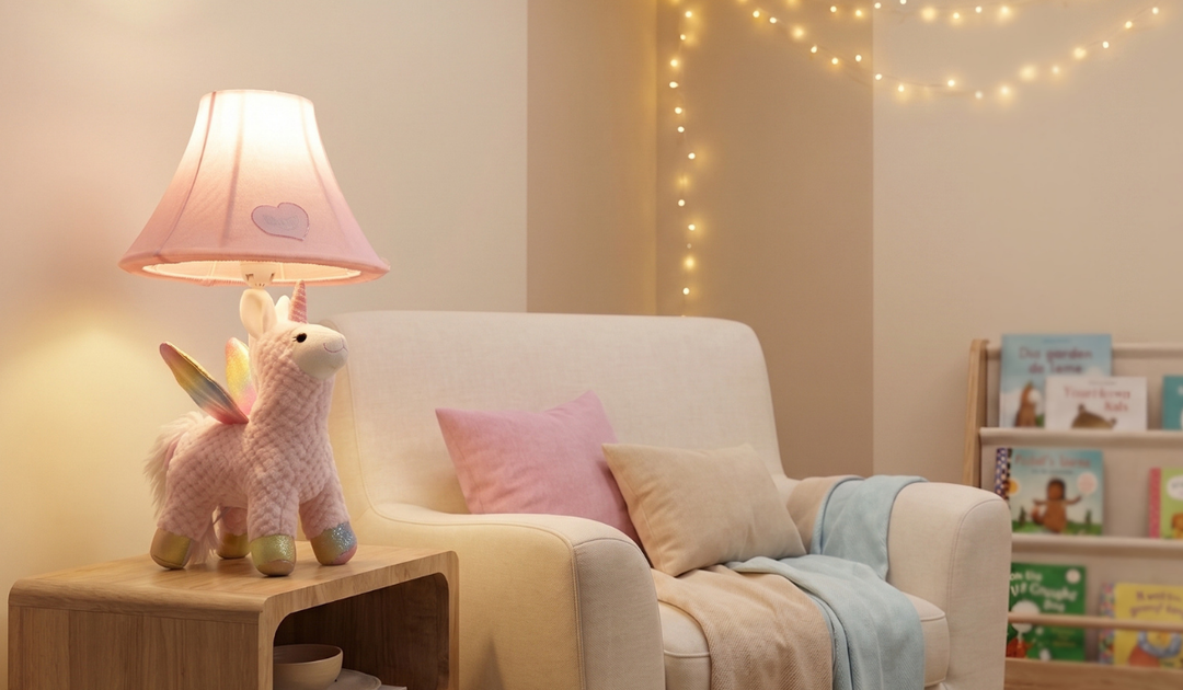 Naturally KIDS pink unicorn table lamp with a warm light on a side table by an armchair and a shelf of picture books