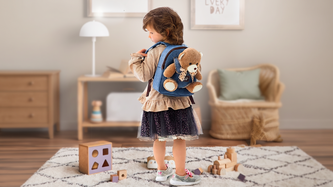A toddler wears a Naturally KIDS small backpack with a removable plush teddy bear in a kids' room